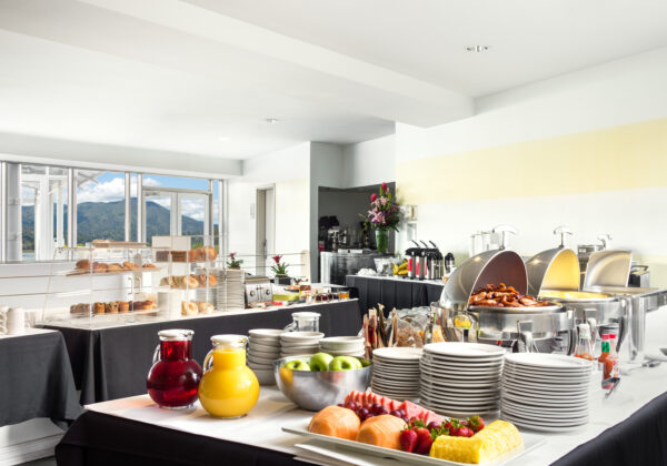 Breakfast buffet on 3 separate tables with fruit, pastries, coffee, eggs, bacon, potatoes, and juices