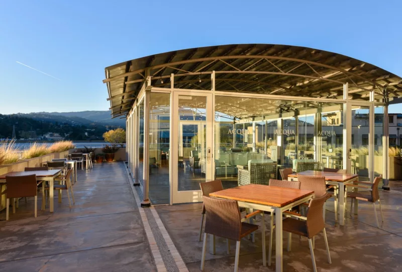 Glassed-in rooftop atrium at sunrise, with tables and chairs on open air patio surrounding the atrium